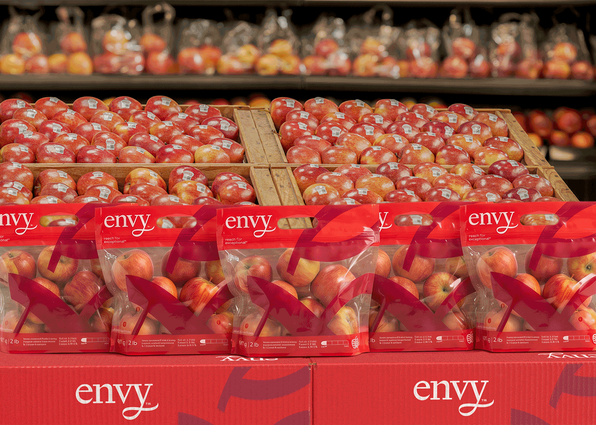 Bulk crates and branded bags of red Envy apples on display in a retail grocery produce department