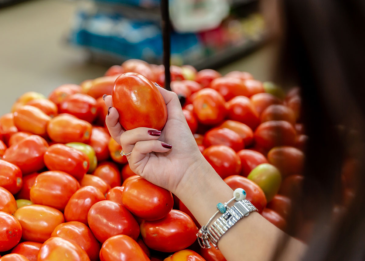 woman shopper holding a tomato near a grocery store retail display