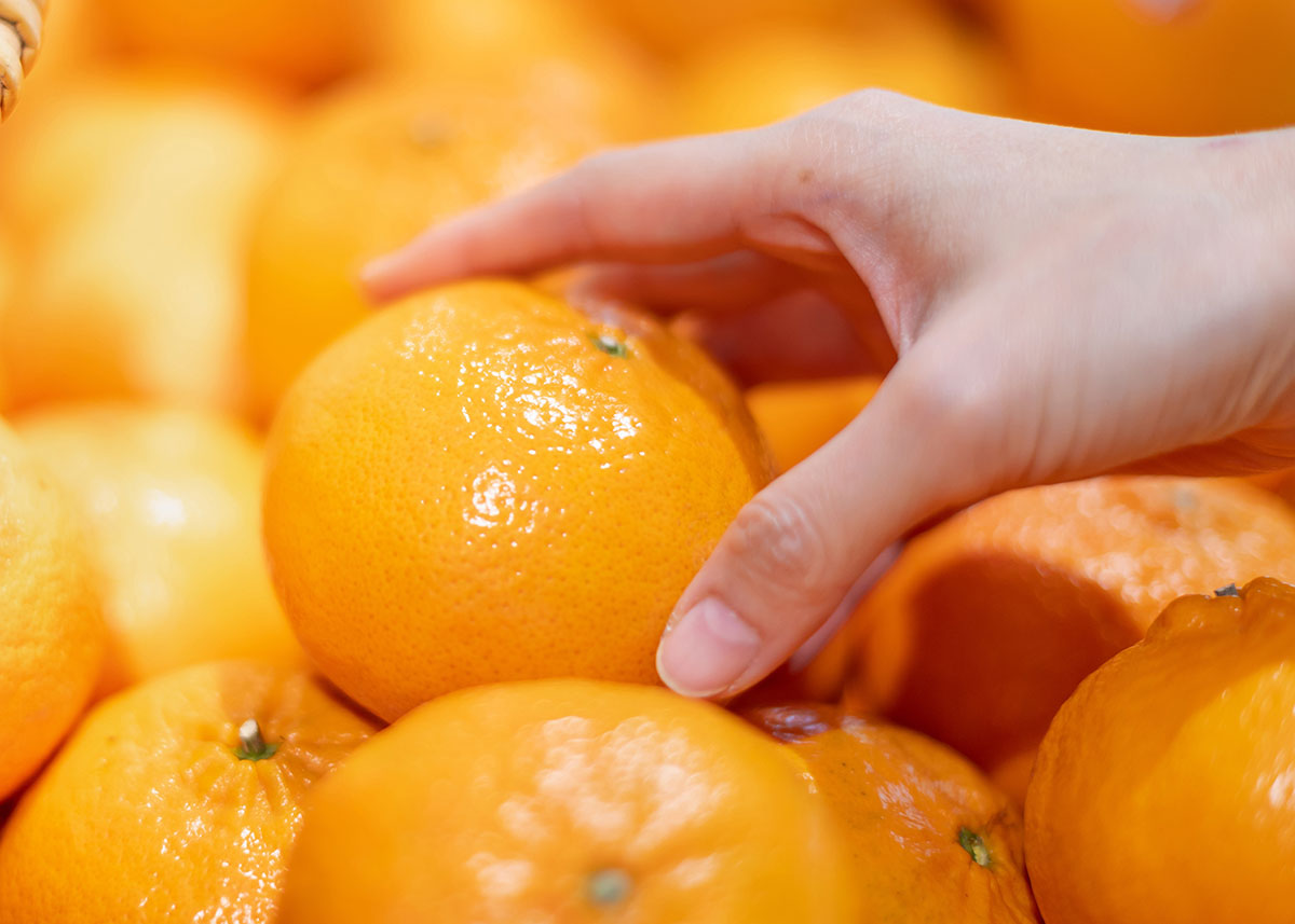 shopper's hand grabbing an orange from a display of oranges