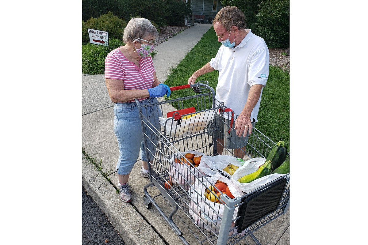 Two people on sidewalk chatting over cart of fresh produce