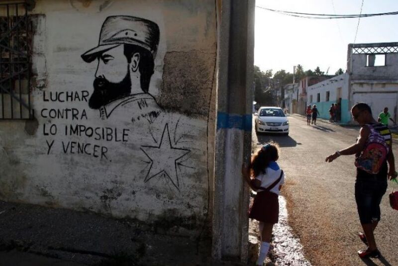 A man walks his daughter from school past a mural of the late Fidel Castro, flanked by a quote from Castro that says in Spanish: "Fight against the impossible and overcome" in Havana, Cuba, Monday, Nov. 28, 2016.