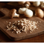 A professional photo of a rustic wooden cutting board on a wooden table. The focus is on a pile of diced mushrooms in the foreground, with whole white mushrooms out of focus in the background.