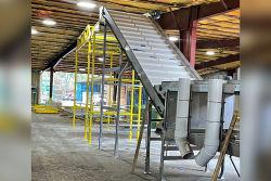 A metal conveyor line slopes at an angle to connect a higher part of the line to the lower part inside a covered building.