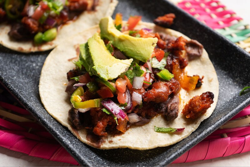 Close up image of a pork chorizo taco on a corn torilla, topped with pico and fresh avocado. 