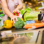 Woman's hands are touching vegetables, such as bell peppers, broccoli and celery, which are on a store checkout line conveyor belt.