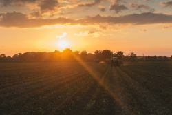 A sun over a field with farm machinery