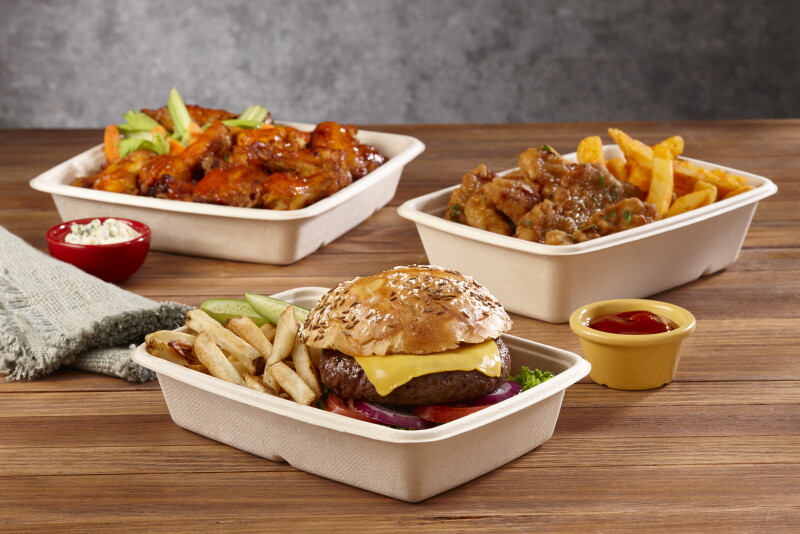 Shown are three containers: One in front holds french fries, pickles and a cheeseburger with lettuce, onion and tomato. The one on the back left holds sauced-covered Buffalo wings with celery and carrots. The one at middle right holds sauced boneless chicken fingers and french fries. There is a small yellow bowl holding sauce next to the containers, which are on a wooden tabletop.