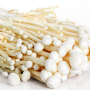 White enoki mushrooms, lying on their sides on a white surface and a white background. The mushrooms are stringy with small white caps.