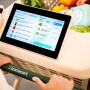A grocery cart is full of groceries and a touchscreen lists the products inside the cart. 