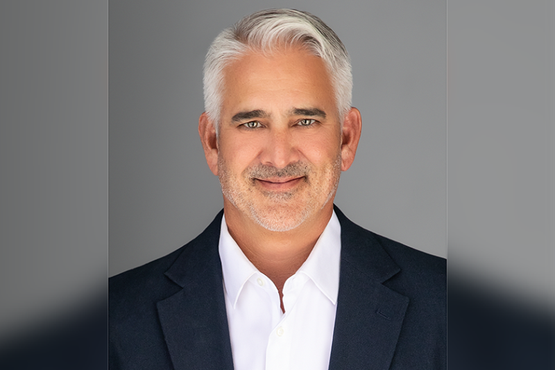 Portrait headshot of a man wearing a dark blazer jacket over a white button-up shirt.
