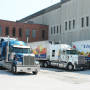 Three tractor trailer trucks, with the FG Lister & Co. Ltd. logo on their trailers, are shown backed toward a brick building.