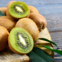 A close-up photo of a cluster of eight brown kiwifruit and two kiwifruit halves on a brown wooden cutting board, which is on a grayish-blue wooden tabletop.