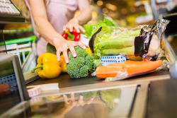 Woman's hands are touching vegetables, such as bell peppers, broccoli and celery, which are on a store checkout line conveyor belt.