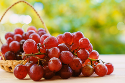 A bunch of red grapes resting on a table, with a basket of more grapes in the background.