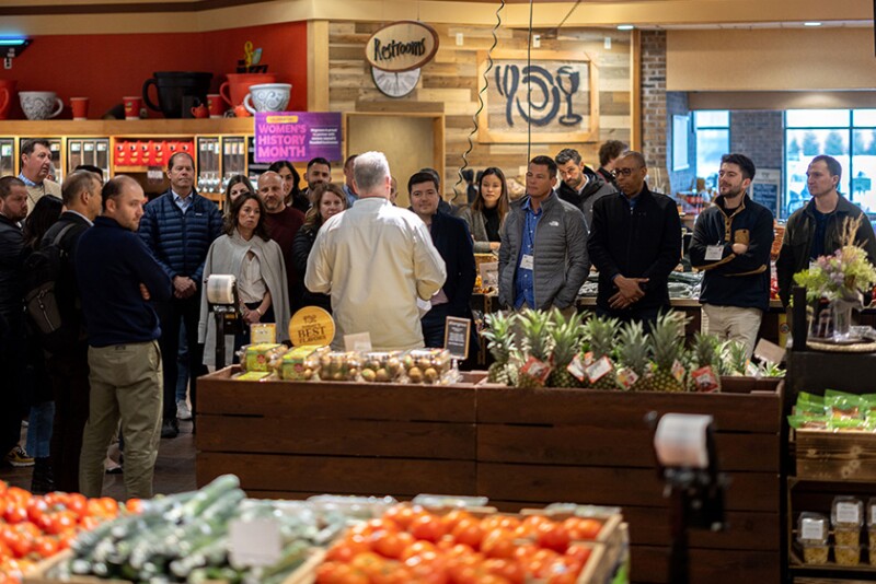 A group of program participants listens to a speaker during a produce retail tour.