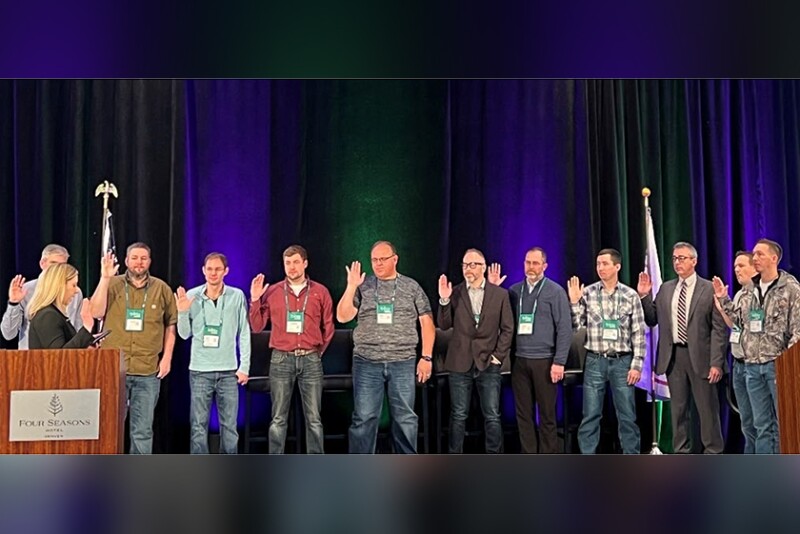 A lineup of people standing on a stage raise their right hands to be sworn in.