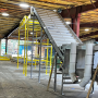 A metal conveyor line slopes at an angle to connect a higher part of the line to the lower part inside a covered building.