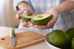 Woman holding a halved avocado in a kitchen.