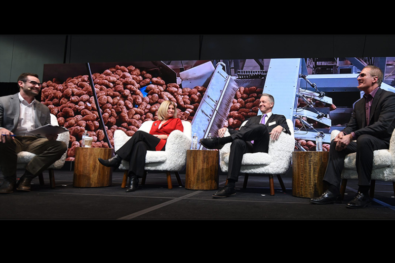 Four people sit in white chairs on a stage, with potatoes arranged decoratively in the background.