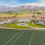 High-angle view of a building an parking lot, with a green field in the foreground and mountains in the background.