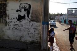A man walks his daughter from school past a mural of the late Fidel Castro, flanked by a quote from Castro that says in Spanish: "Fight against the impossible and overcome" in Havana, Cuba, Monday, Nov. 28, 2016.