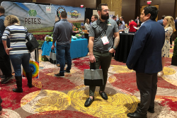 Two men stand in the right foreground speaking to each other. Behind them, other people talk to people at booths.