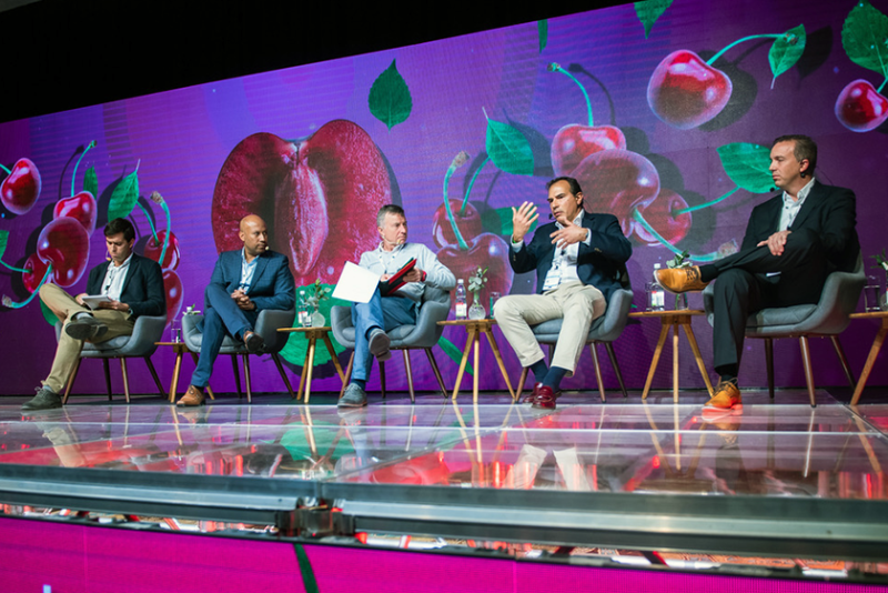 Five men sit on a stage talking to a crowd
