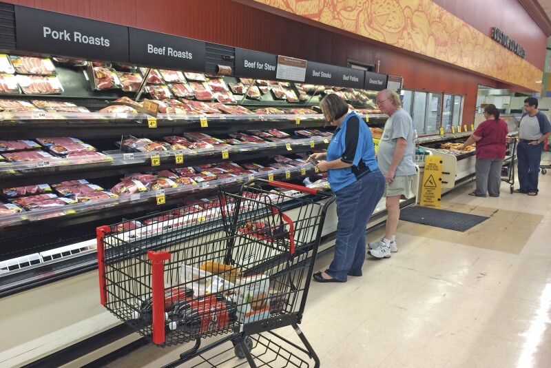Consumers selecting meat from the meat case at a grocery store. 
