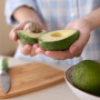Woman holding a halved avocado in a kitchen.