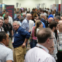 A wide shot of a crowd of people visiting booths on a trade show floor.