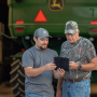 Two men with a tablet in front of a John Deere vehicle.