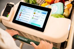 A grocery cart is full of groceries and a touchscreen lists the products inside the cart. 
