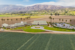 High-angle view of a building an parking lot, with a green field in the foreground and mountains in the background.