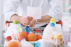 Man with shopping list standing with grocery cart.