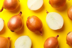 Whole and sliced onions on yellow background
