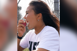 A profile view of Sky Brown, wearing a white T-shirt, facing to the left and about to bite into a Rockit apple.