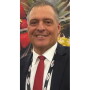 A smiling close up photo of a man in a suit with strawberries and a pineapple in the background.