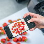 Hand holding a smartphone to take a photo of strawberries