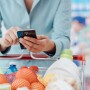 Shopper checking smartphone over full grocery cart