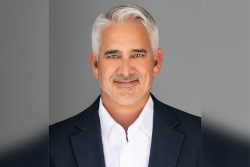 Portrait headshot of a man wearing a dark blazer jacket over a white button-up shirt.