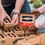 Two people grabbing cartons of strawberries from a stack