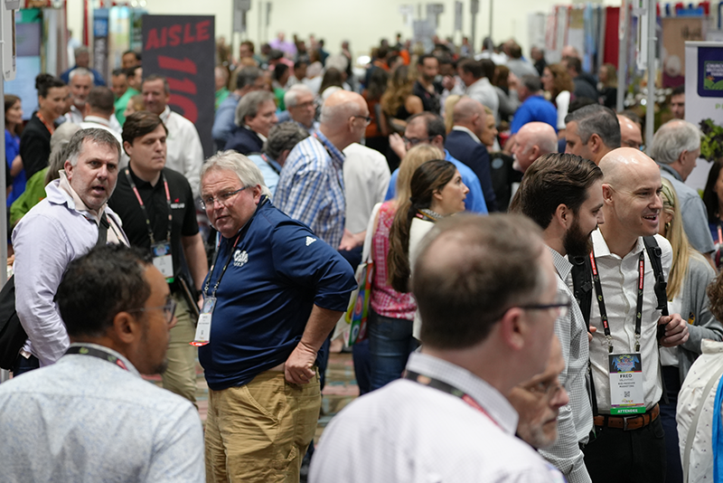 A wide shot of a crowd of people visiting booths on a trade show floor.