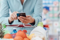 Shopper checking smartphone over full grocery cart