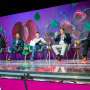 Five men sit on a stage talking to a crowd