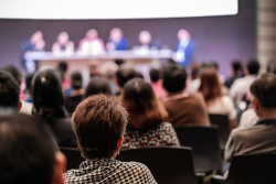 Stock photo of conference crowd facing speakers on a stage