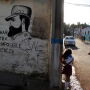 A man walks his daughter from school past a mural of the late Fidel Castro, flanked by a quote from Castro that says in Spanish: "Fight against the impossible and overcome" in Havana, Cuba, Monday, Nov. 28, 2016.