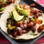 Close up image of a pork chorizo taco on a corn torilla, topped with pico and fresh avocado. 