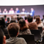 Stock photo of conference crowd facing speakers on a stage